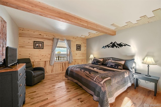 bedroom with beam ceiling, light wood-type flooring, and wood walls