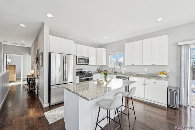 kitchen featuring appliances with stainless steel finishes, light stone counters, a kitchen island, dark hardwood / wood-style floors, and white cabinetry