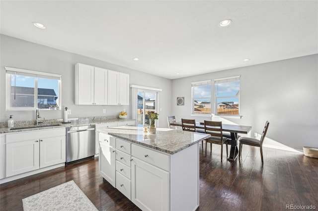 kitchen with sink, stainless steel dishwasher, a kitchen island, light stone counters, and white cabinetry