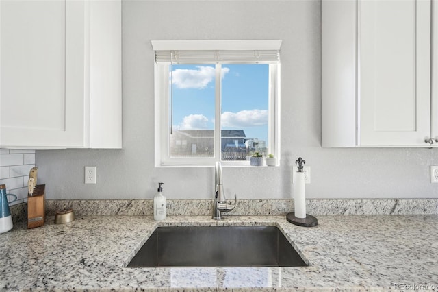 details with white cabinets, backsplash, light stone counters, and sink