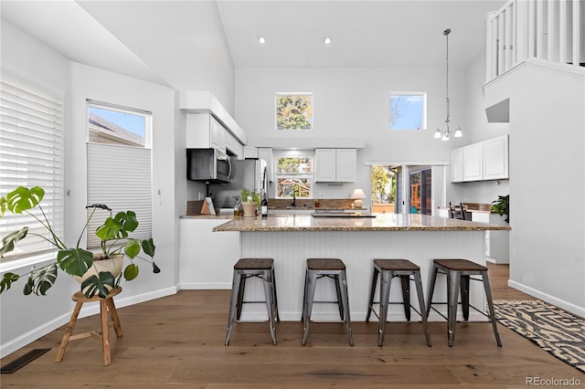 kitchen featuring stainless steel microwave, a high ceiling, white cabinets, a breakfast bar, and light stone countertops