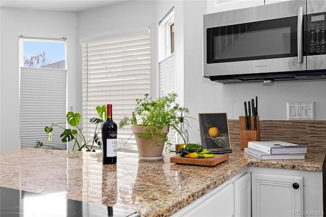 kitchen with stainless steel microwave, tile counters, white cabinets, and decorative backsplash