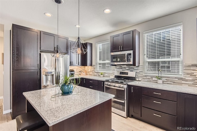 3795 Depew St Unit D, Wheat Ridge, CO 80212 - kitchen featuring appliances with stainless steel finishes, light wood-type flooring, decorative backsplash, light stone countertops, and a kitchen island
