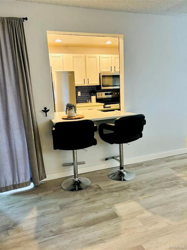 kitchen featuring light wood-style flooring, baseboards, a kitchen breakfast bar, appliances with stainless steel finishes, and tasteful backsplash