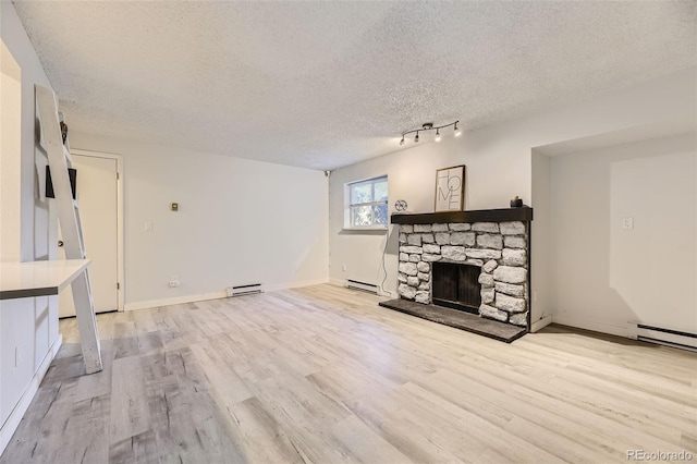 unfurnished living room featuring a textured ceiling, a stone fireplace, baseboard heating, and light wood-style flooring