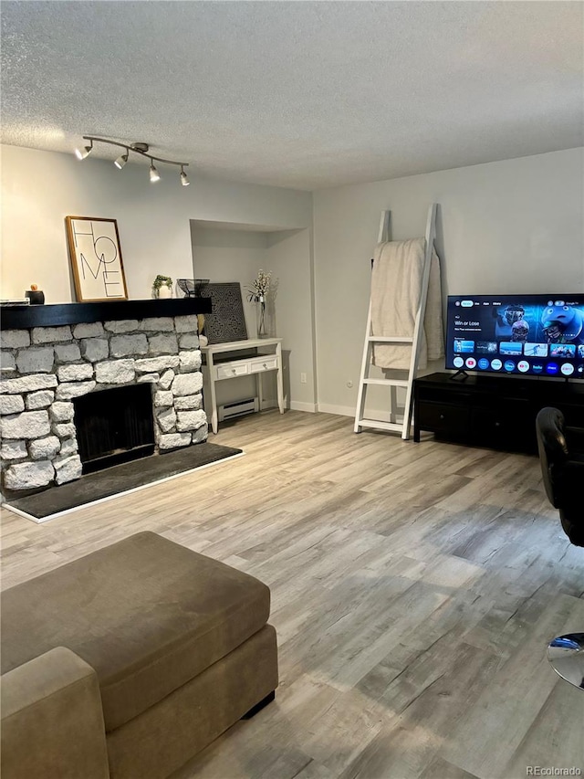 living area with a textured ceiling, a stone fireplace, a baseboard radiator, wood finished floors, and baseboards