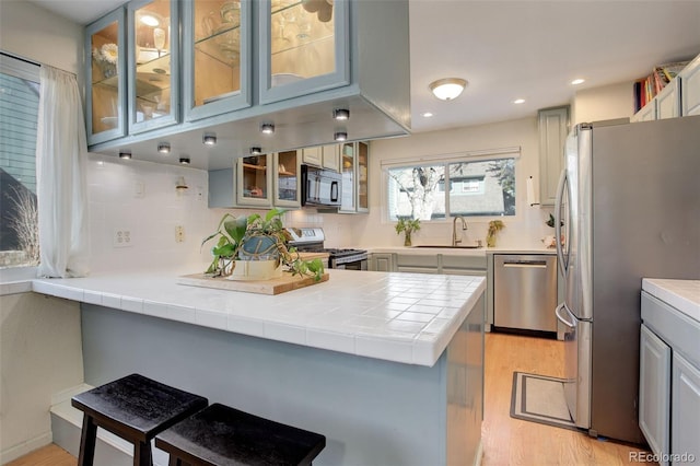 kitchen featuring a peninsula, a sink, decorative backsplash, light wood-style floors, and appliances with stainless steel finishes