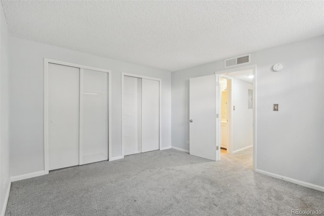 unfurnished bedroom featuring two closets, a textured ceiling, and light colored carpet