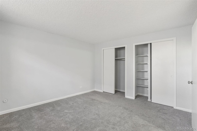 unfurnished bedroom with carpet, a textured ceiling, and two closets