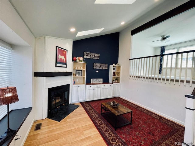 living room with a large fireplace, visible vents, baseboards, and light wood finished floors