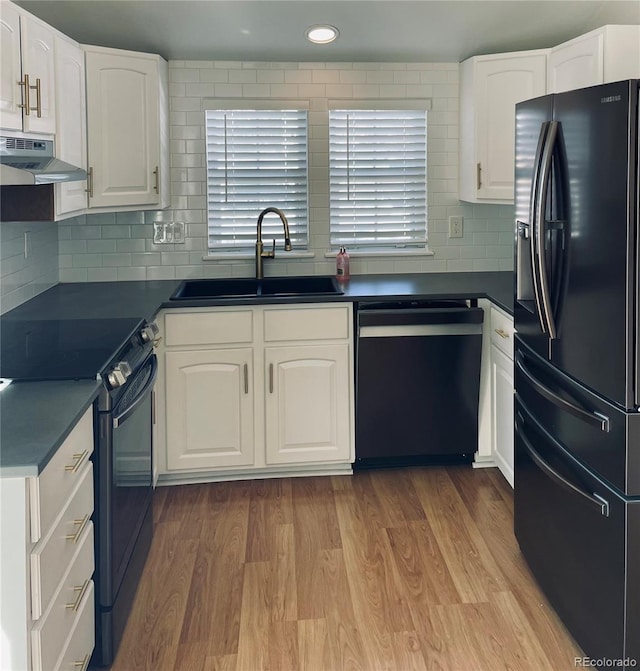 kitchen with light wood finished floors, dark countertops, under cabinet range hood, black appliances, and a sink