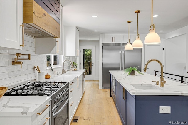 kitchen with light stone counters, decorative light fixtures, white cabinets, appliances with stainless steel finishes, and sink