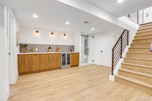 bar with wine cooler, light hardwood / wood-style floors, and sink