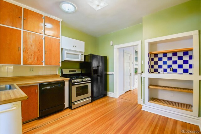 kitchen with black appliances, sink, tasteful backsplash, and light hardwood / wood-style floors