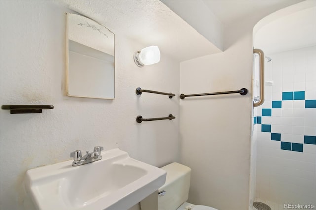 bathroom with toilet, tiled shower, and sink