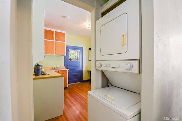 washroom featuring stacked washer / dryer, sink, and light hardwood / wood-style flooring