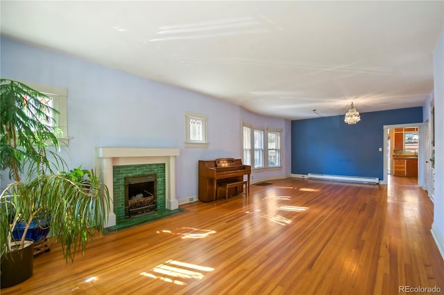 unfurnished living room featuring baseboard heating, wood-type flooring, a notable chandelier, and a fireplace