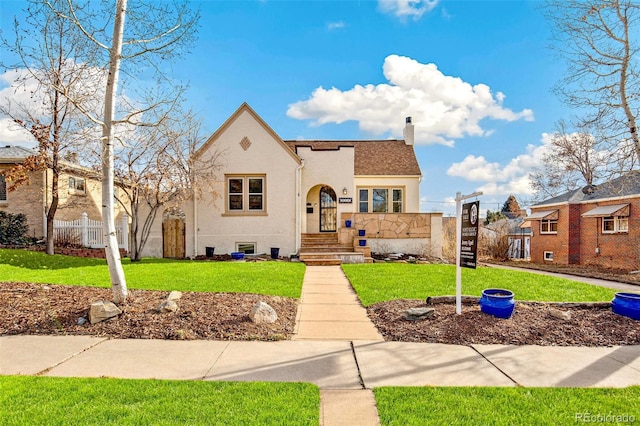 view of front of house with stucco siding, a chimney, fence, and a front yard