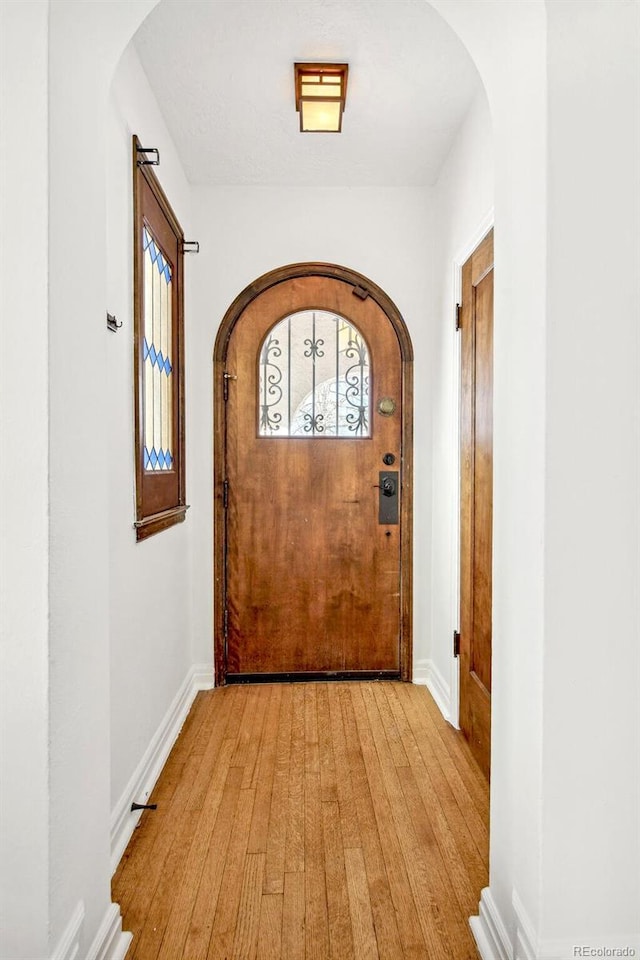 entryway with light wood-style flooring, arched walkways, and baseboards