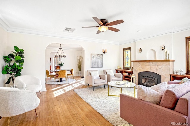 living room with visible vents, arched walkways, ornamental molding, wood finished floors, and a fireplace