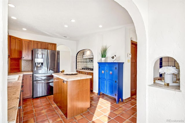 kitchen featuring a kitchen island, arched walkways, backsplash, and stainless steel fridge with ice dispenser