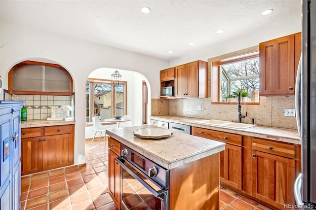 kitchen with stainless steel appliances, a sink, a kitchen island, light countertops, and brown cabinetry