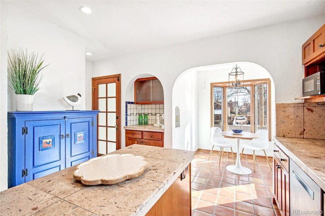 kitchen featuring brown cabinetry, tile countertops, black microwave, backsplash, and recessed lighting