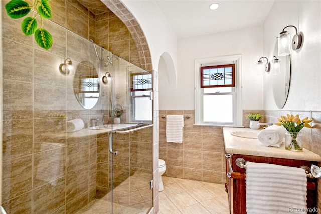 full bath with tile walls, toilet, a shower stall, vanity, and tile patterned flooring