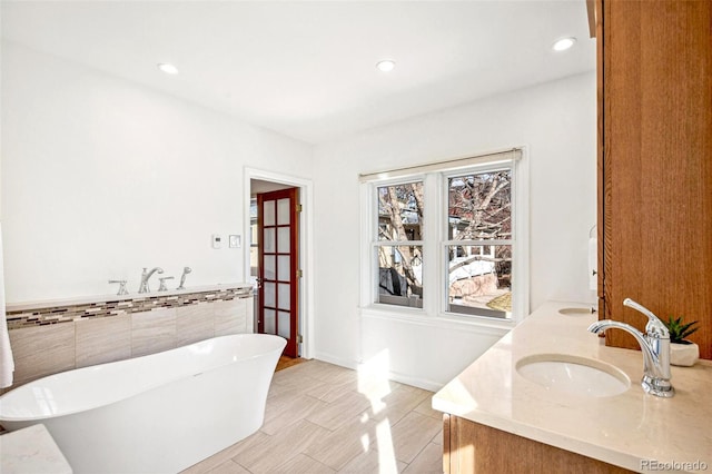 bathroom with double vanity, a soaking tub, a sink, and recessed lighting