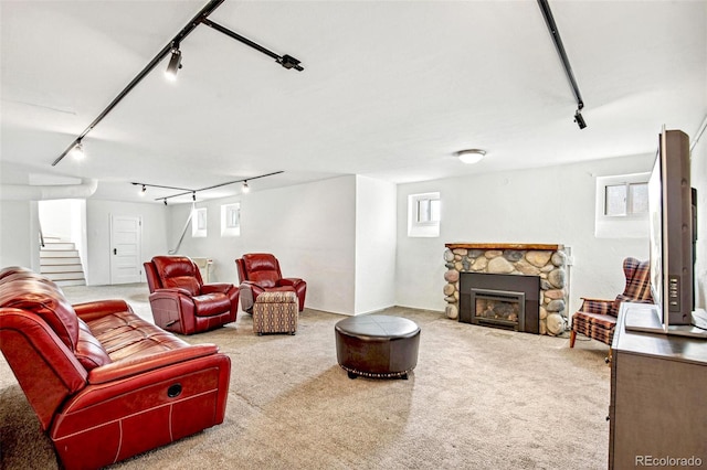 carpeted living room featuring a stone fireplace, stairway, and track lighting