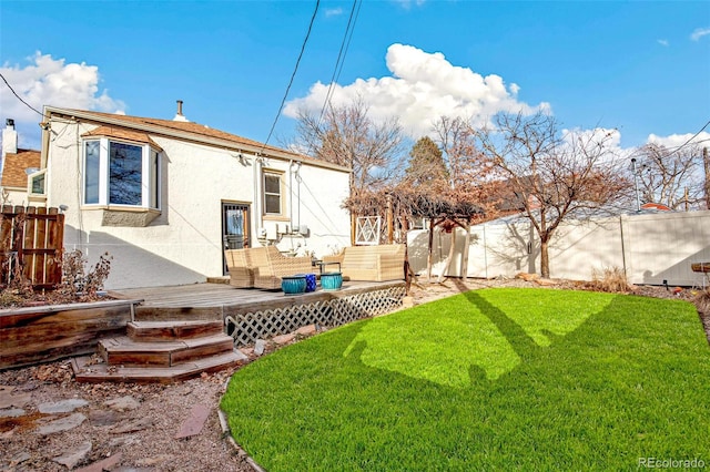 rear view of house featuring a lawn, a fenced backyard, a wooden deck, and stucco siding