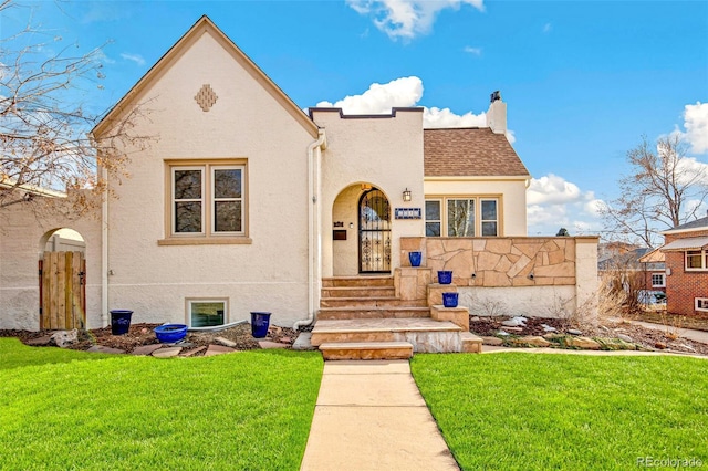 view of front of house featuring a shingled roof, a front yard, a chimney, and stucco siding