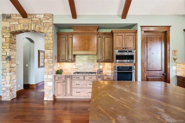 2480 Castle Butte Dr, Castle Rock, CO 80109 - kitchen featuring stainless steel gas cooktop, arched walkways, dark wood-style flooring, decorative backsplash, and wall chimney range hood