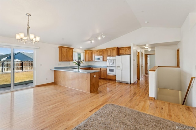 kitchen featuring light wood finished floors, lofted ceiling, an inviting chandelier, white appliances, and a peninsula