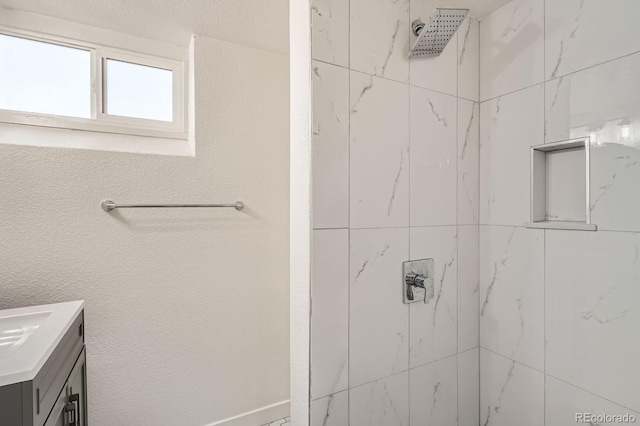 full bathroom featuring a tile shower, vanity, and a textured wall