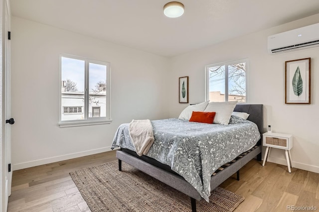 bedroom with a wall unit AC, light wood-style flooring, and baseboards