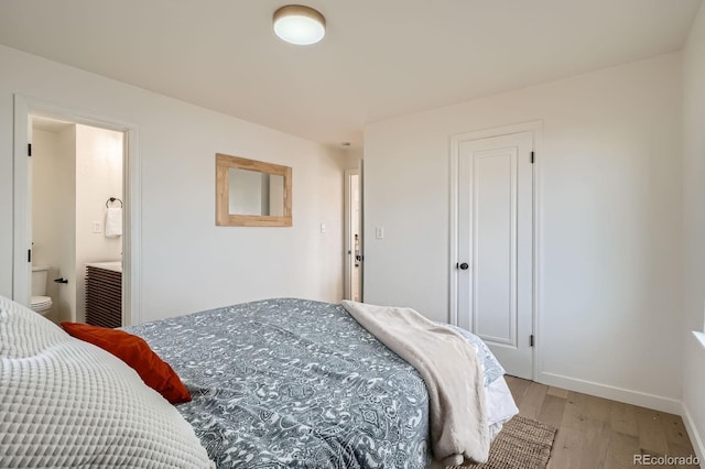 bedroom with connected bathroom, baseboards, and light wood finished floors