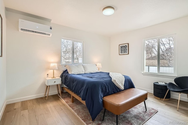 bedroom featuring light wood-style flooring, multiple windows, baseboards, and a wall mounted air conditioner