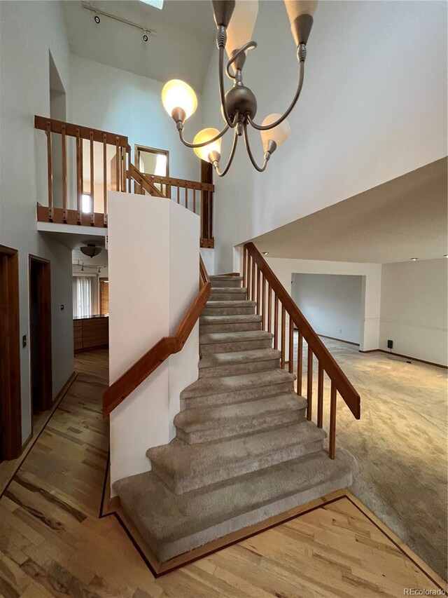 stairway featuring a high ceiling, an inviting chandelier, wood finished floors, a skylight, and rail lighting
