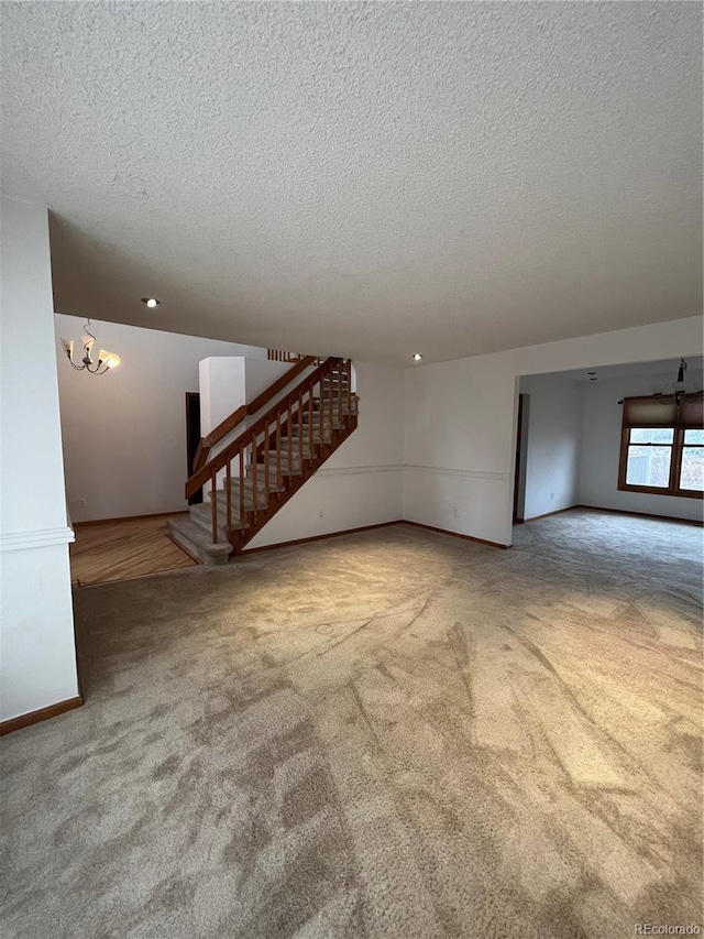 unfurnished living room with a notable chandelier, baseboards, a textured ceiling, stairs, and carpet