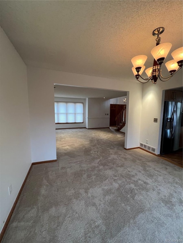 spare room with a textured ceiling, carpet floors, a chandelier, stairway, and baseboards