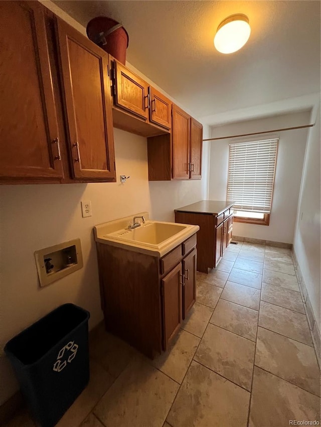 kitchen featuring brown cabinetry, light tile patterned floors, baseboards, and a sink