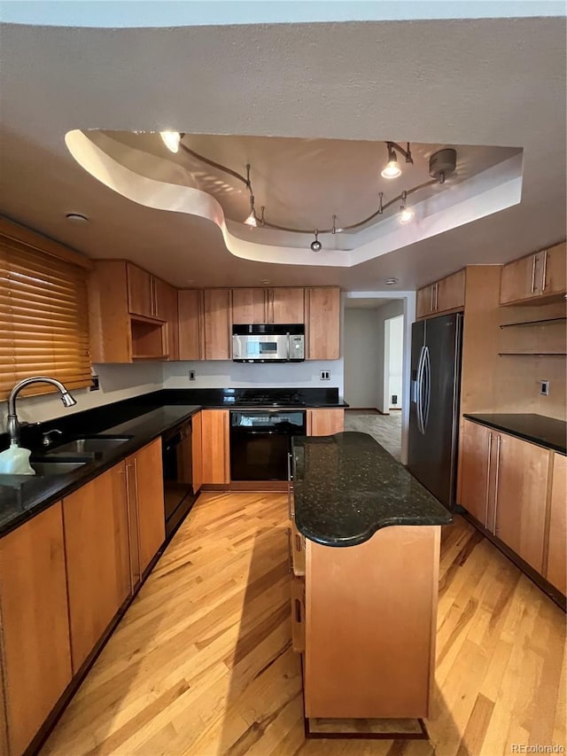 kitchen featuring a tray ceiling, light wood-style flooring, black appliances, a kitchen island, and a sink