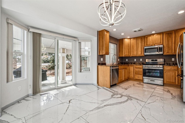 kitchen with stainless steel appliances, dark countertops, brown cabinetry, and decorative light fixtures