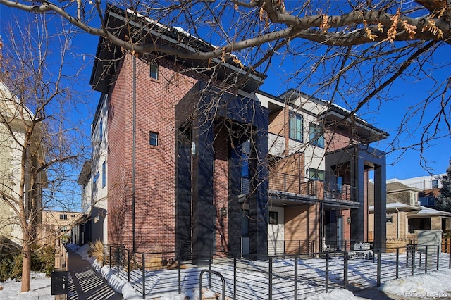 view of snowy exterior featuring a fenced front yard and brick siding