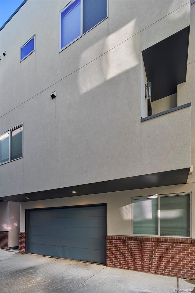 view of property exterior featuring a garage, stucco siding, concrete driveway, and brick siding