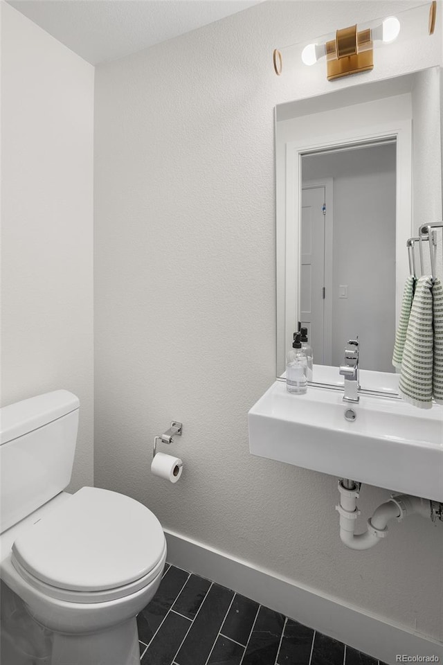 half bath featuring tile patterned flooring, a sink, toilet, and baseboards