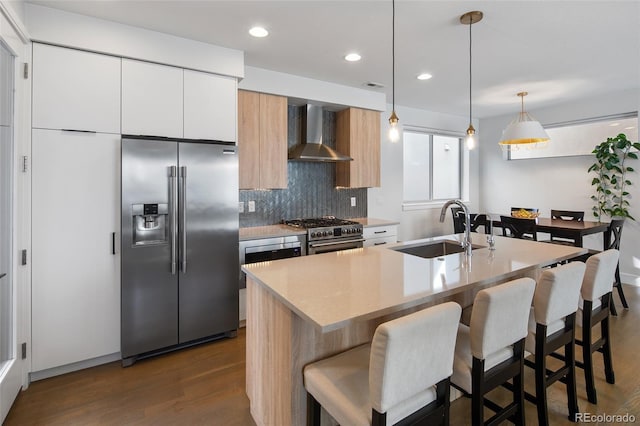 kitchen with tasteful backsplash, premium appliances, a breakfast bar area, wall chimney range hood, and a sink