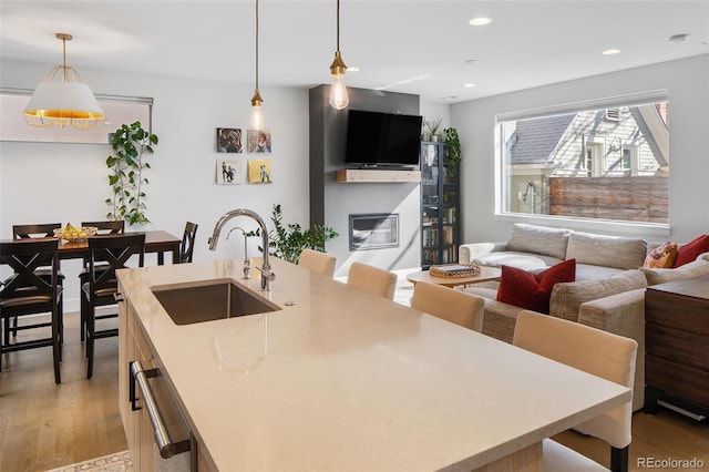 kitchen with pendant lighting, recessed lighting, light wood-style floors, a sink, and an island with sink