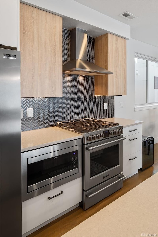 kitchen with stainless steel appliances, light countertops, visible vents, wall chimney range hood, and modern cabinets